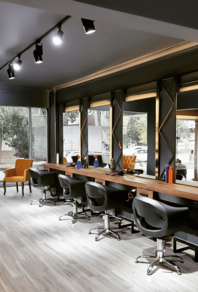 Modern hair salon interior with styling chairs, large mirrors, wooden counters, and bright track lighting. Title:
