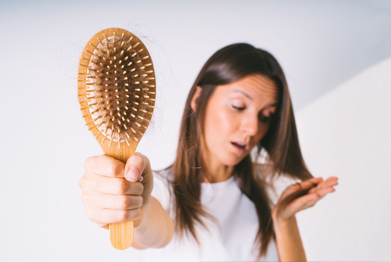 Woman holding hairbrush with visible hair fall strands showing hair loss problem