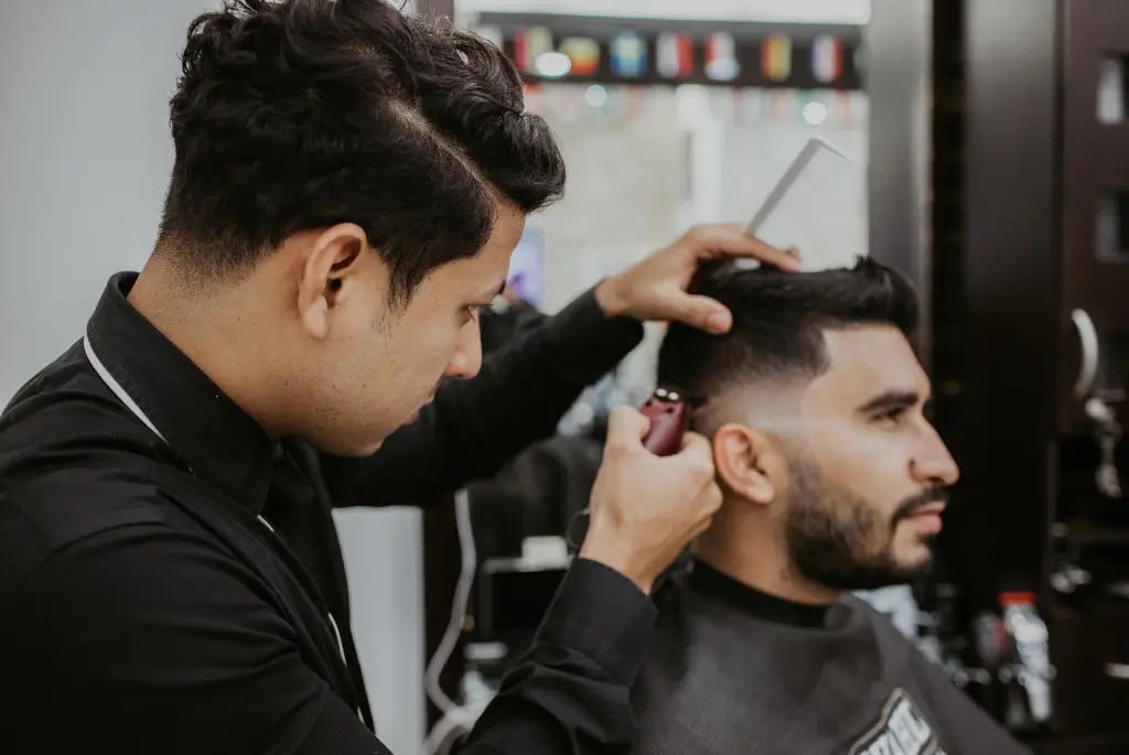 Professional barber trimming client’s hair with electric clipper in modern salon